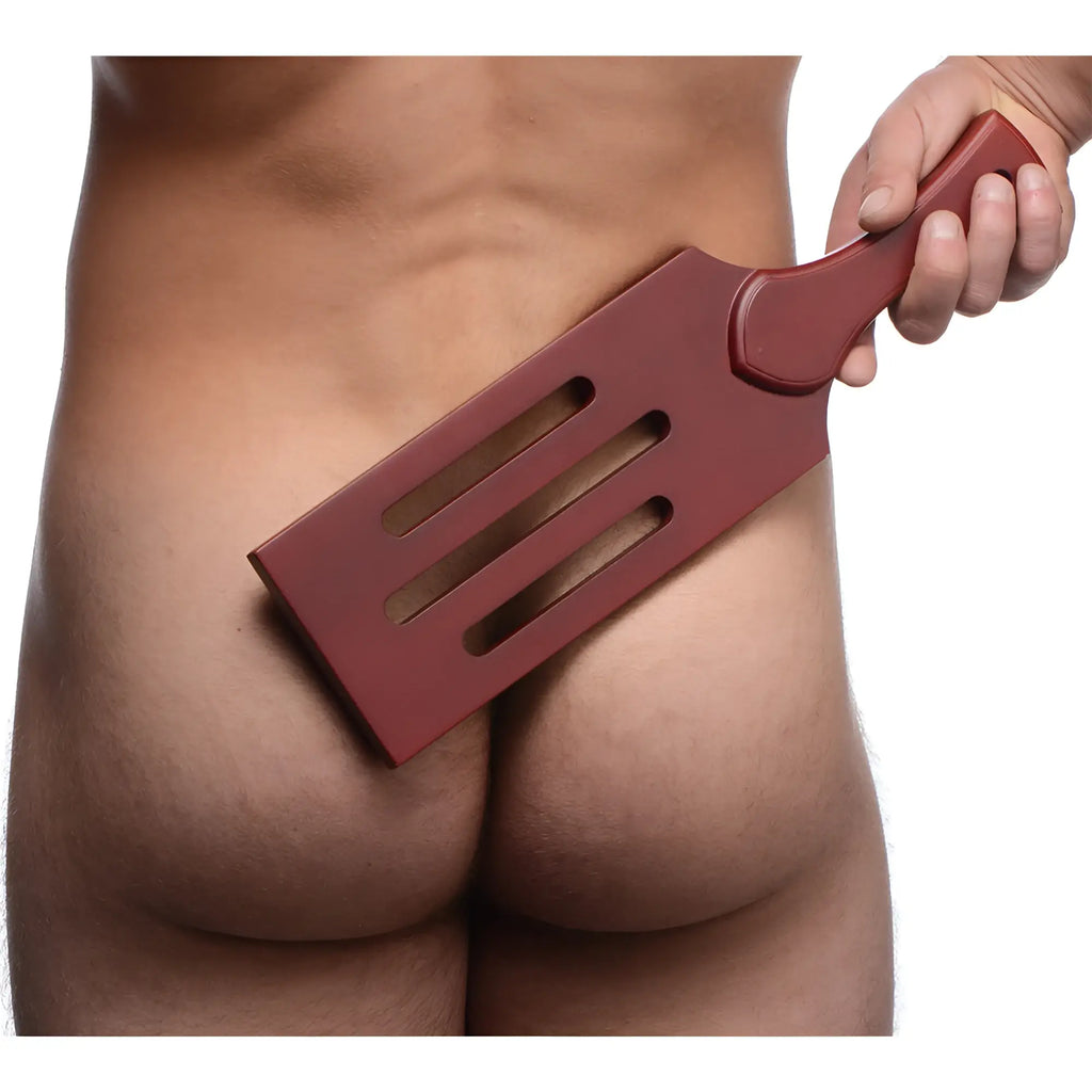 Red plastic masters wooden paddle with three elongated slots and contoured handle for spanking use