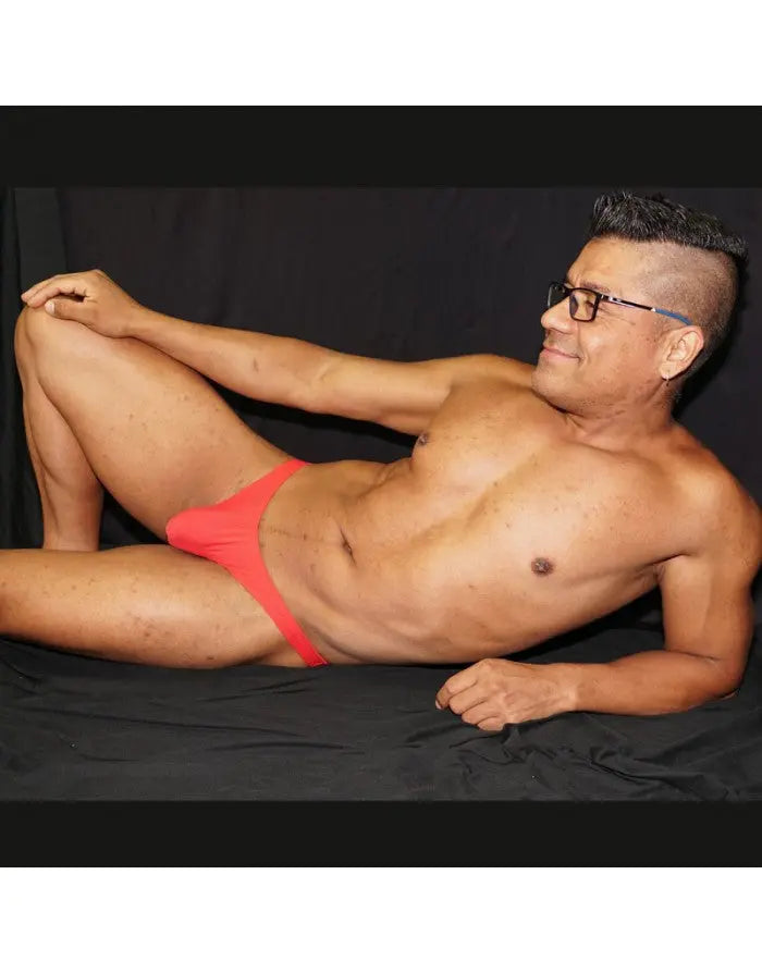 Red micro bikini underwear made of soft fabric shown on a model reclining against a black background by Arroyman.