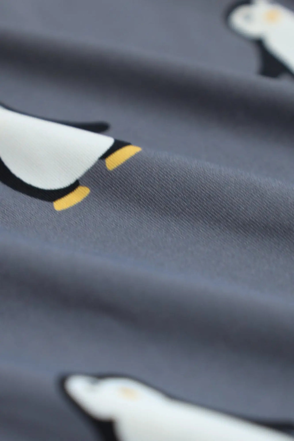 Men’s boxer briefs in gray fabric with a repeating pattern of cartoon penguins with white bodies and yellow feet