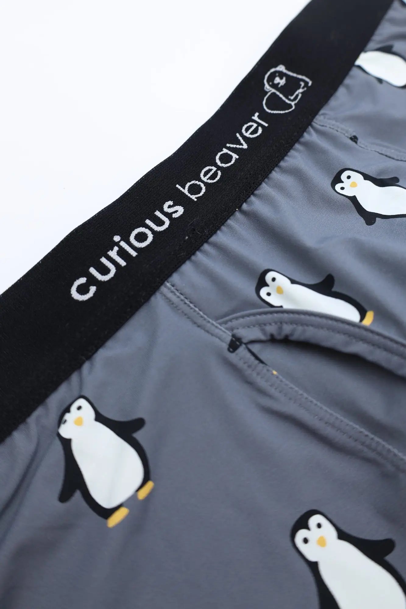 Gray men’s boxer briefs with playful penguin pattern and black elastic waistband featuring curious beaver brand name