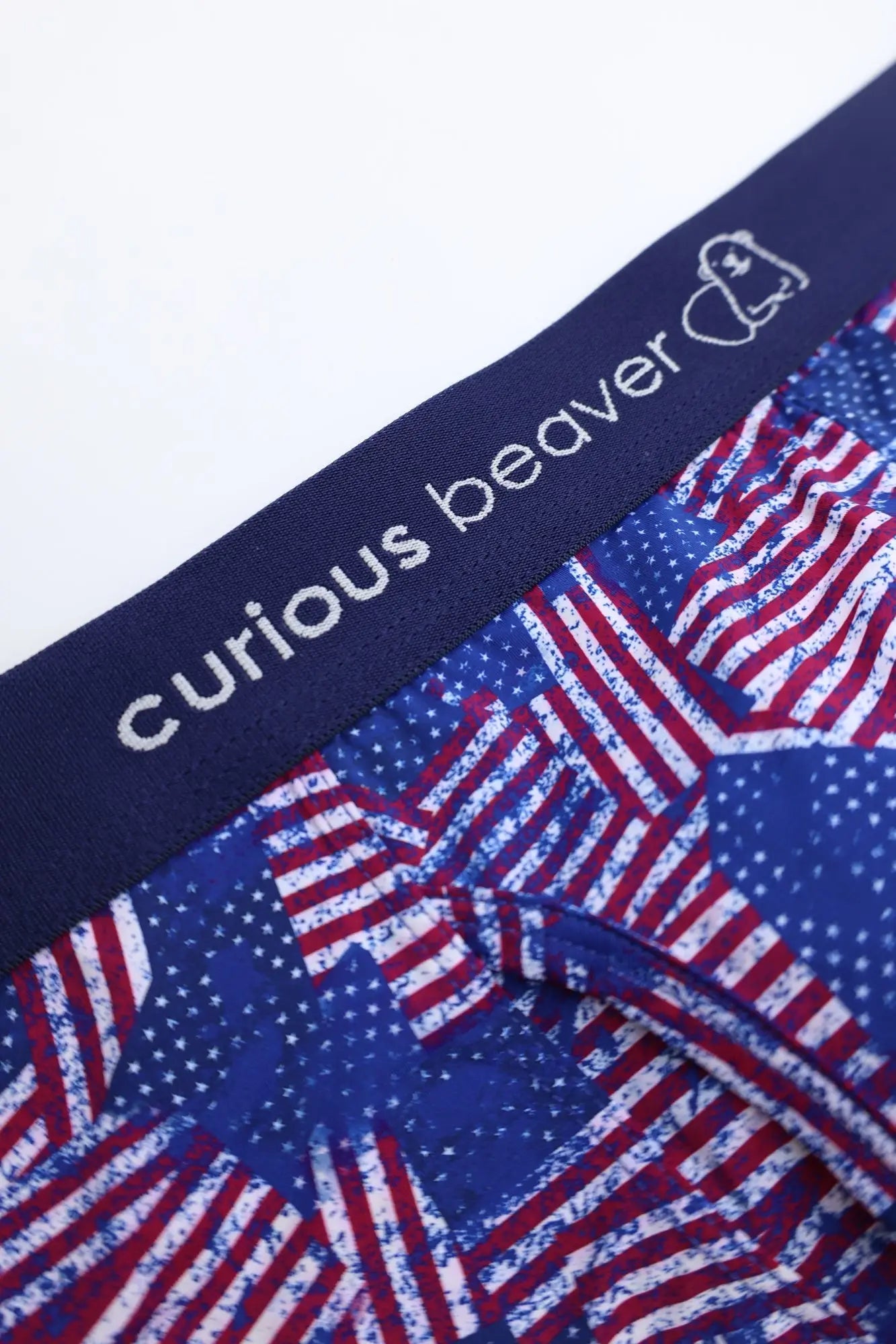 Men’s boxer briefs with blue and red USA flag pattern and navy elastic waistband featuring curious beaver branding