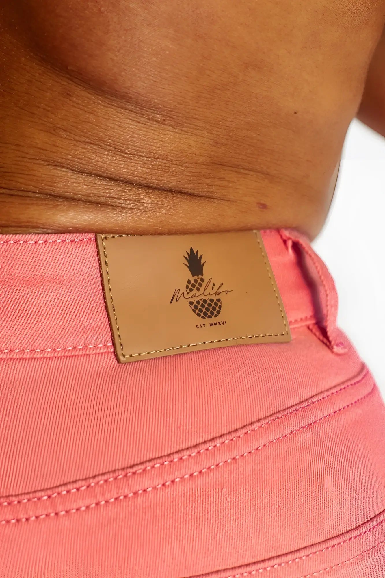 Men’s hot pink coral-colored denim shorts with tan leather patch featuring pineapple logo and mellif branding back view