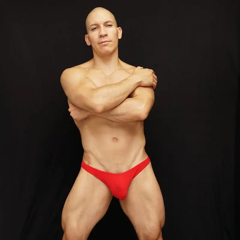 Red bikini underwear by Arroyman featuring a snug fit and minimal coverage modeled by a man against a black background.