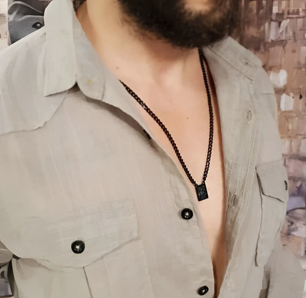 Men’s stainless steel black scapular necklace with rectangular engraved pendant worn by man in light shirt
