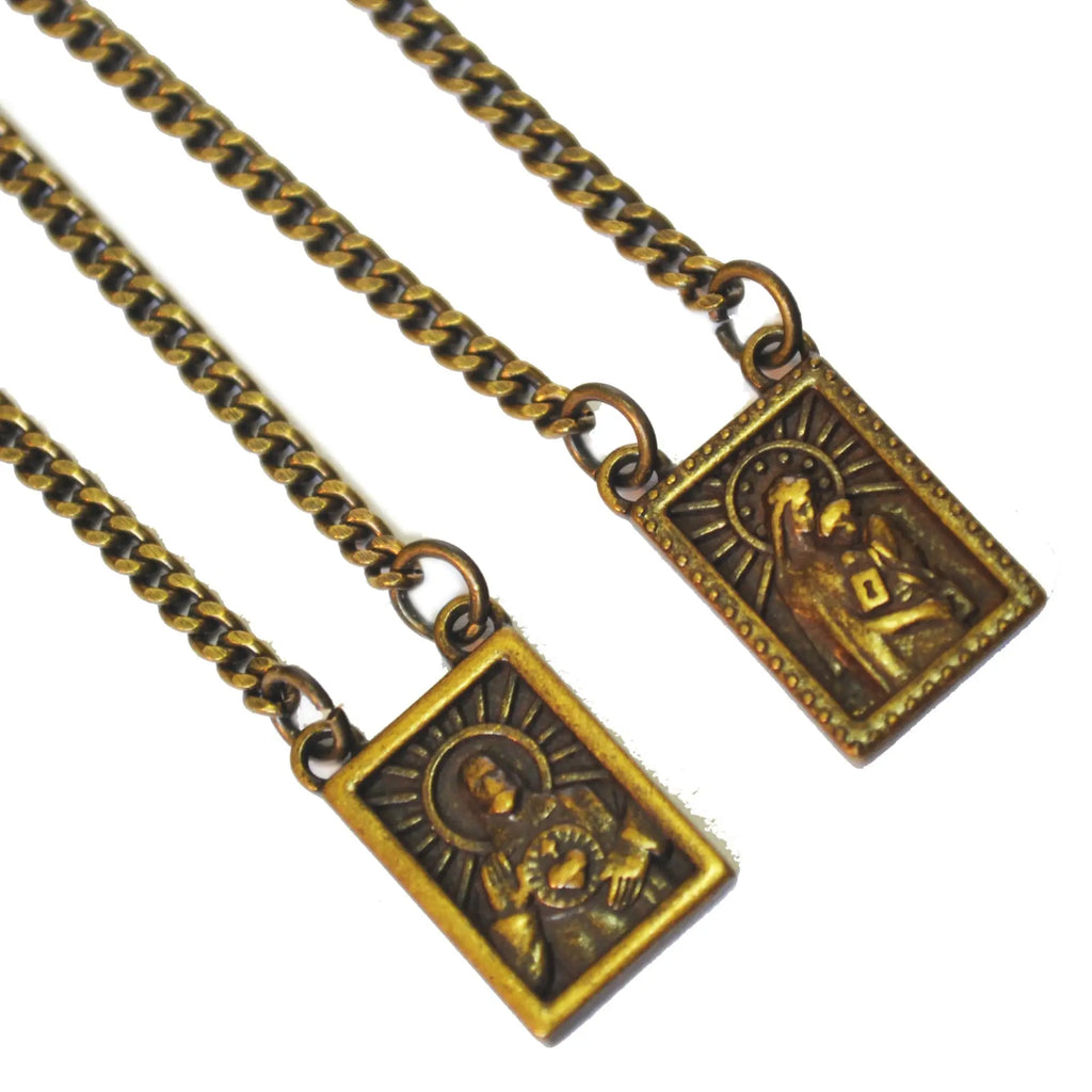 Two antique brass-colored rectangular prayer medals with embossed religious figures on men’s stainless steel scapular