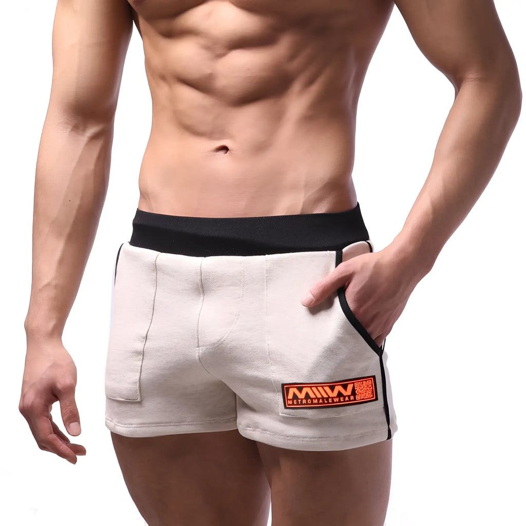 Beige cotton metro malewear sport shorts with black elastic waistband and side trim featuring an orange logo patch
