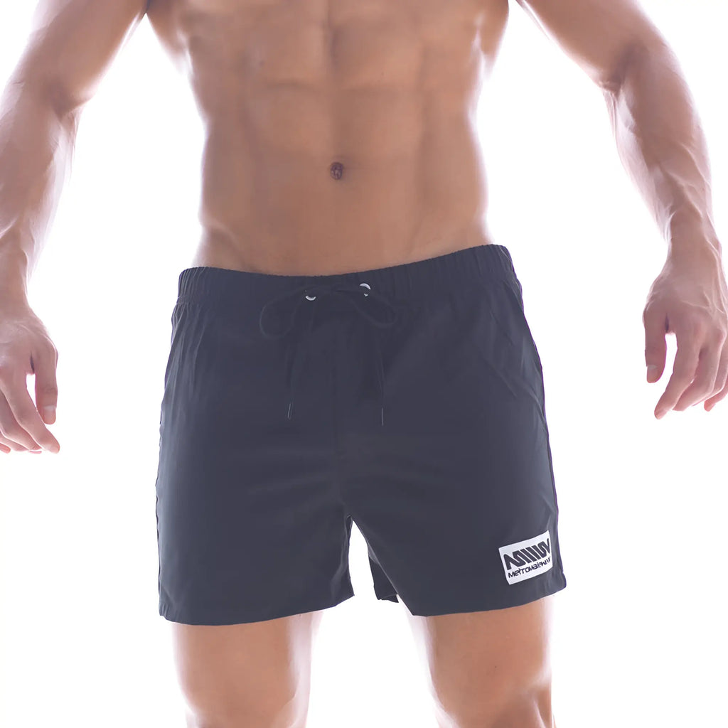 Black athletic swim shorts with drawstring waistband and white rectangular logo patch on lower right leg by metromalewear