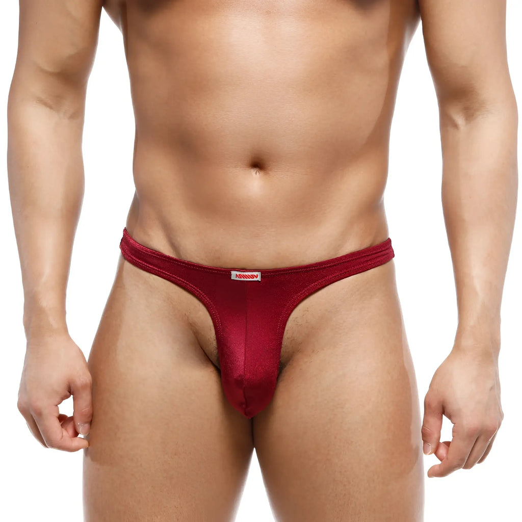 A sleek deep red mens thong made of smooth stretchy fabric with subtle sheen and white brand tag at waistband