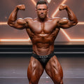 A muscular man wearing black MetroMaleWear MetroMuscleWear Cadena silver chain belt competition briefs