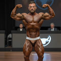 A muscular man wearing a white and gold metroMuscleWear cortina bronze muscle trunk brief with muscle branded waistband