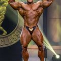 A muscular bodybuilder wearing black and gold metallic textured MetroMaleWear MetroMuscleWear Fortuna competition briefs