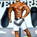A muscular man wearing white MetroMaleWear MetroMuscleWear Mark Physique board shorts with a small logo