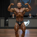 A muscular man flexing in black MetroMaleWear MetroMuscleWear Muscle Trunk briefs with a white bull logo at contest