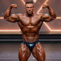 A muscular man flexing in royal blue and black striped MetroMaleWear MetroMuscleWear competition briefs on stage
