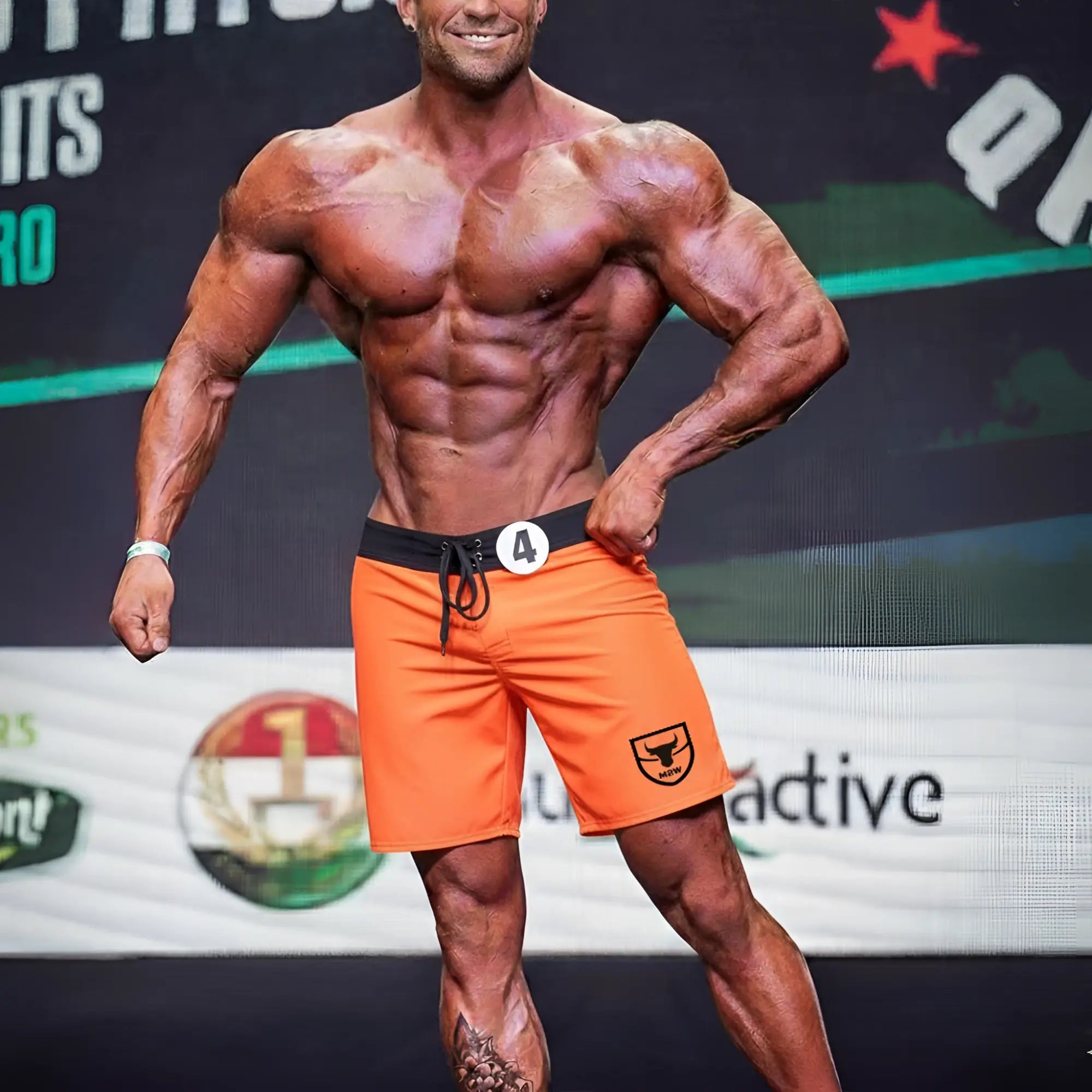 MetroMaleWear physique board short orange with black waistband and drawstring featuring shield logo on lower right leg