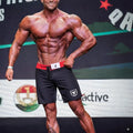 Black athletic MetroMaleWear physique board shorts with red waistband and white logo on left leg designed for performance