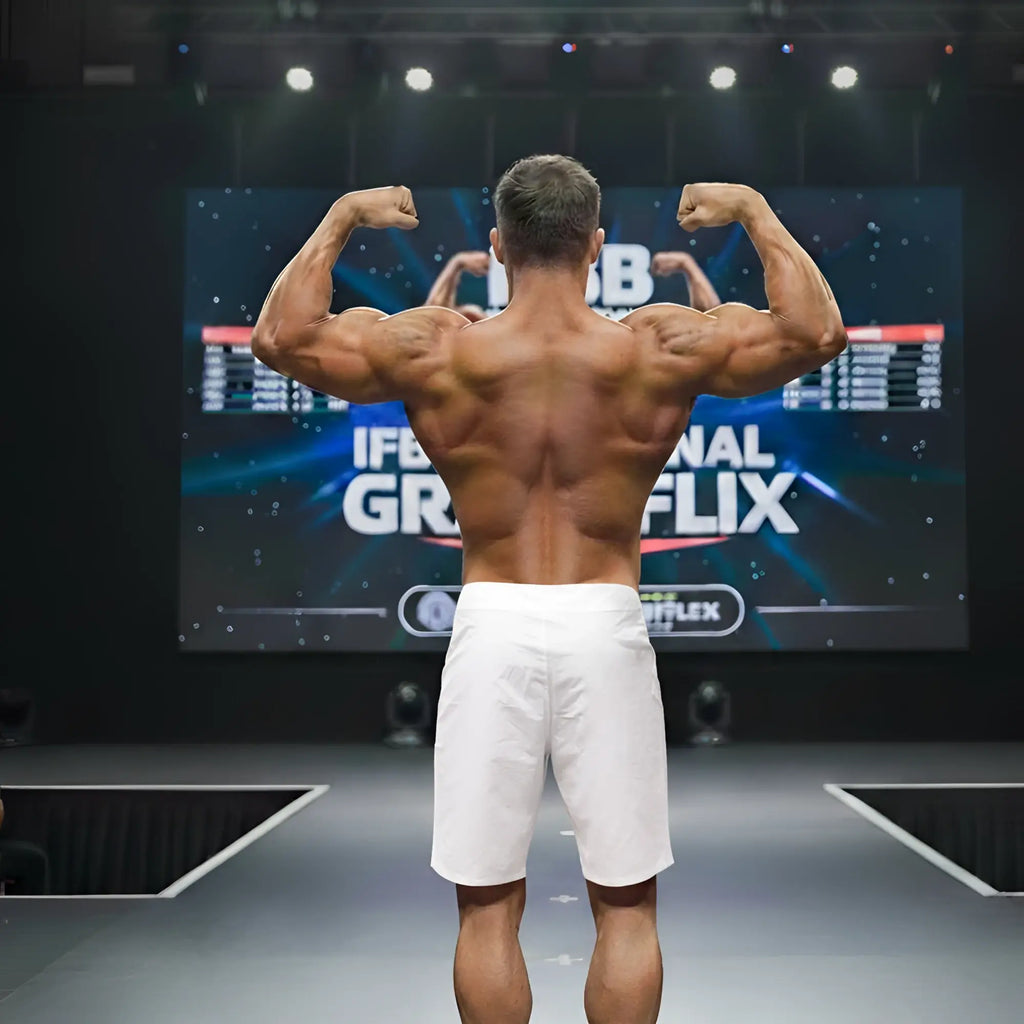 A muscular man shows defined back muscles wearing metro malewear physique board short white on stage from back side