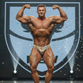 A muscular man wearing metroMalewear posingwear hologram gold shiny patterned briefs with number 38 on his hip