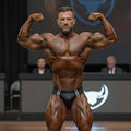 A muscular man flexing in black leather MetroMaleWear versatile swim briefs with white stripes on stage