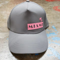 Gray miami baseball cap with pink patch featuring black lettering and two palm trees above the word miami