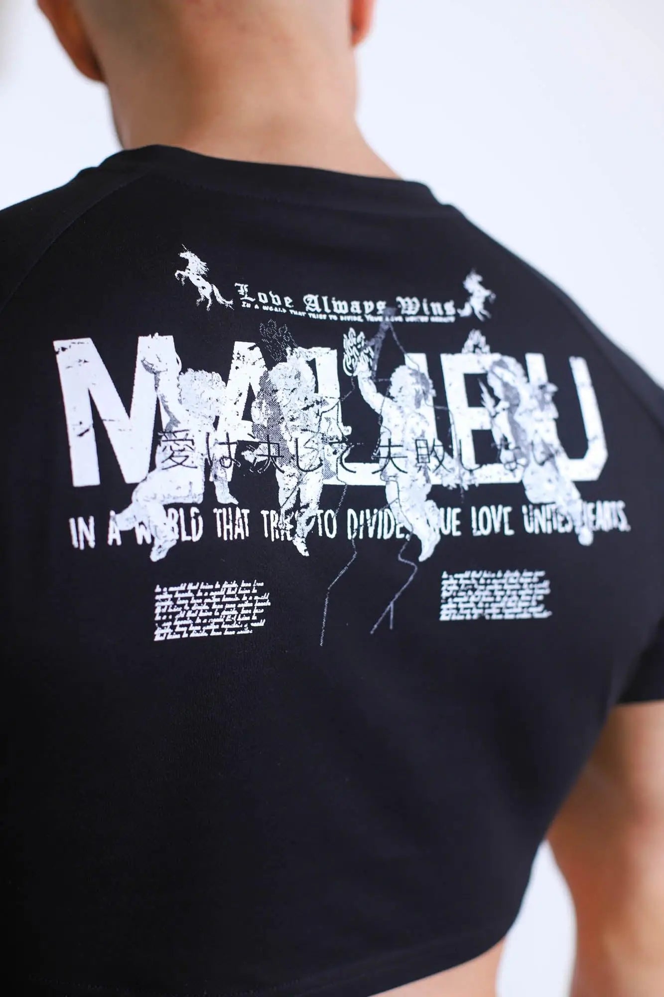 Black muscle-fit crop tee with short sleeves and bold white mariqueu graphic featuring stylized figures and bilingual text