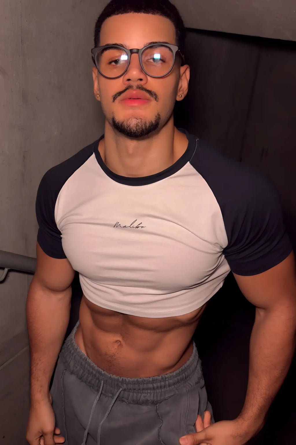 A man wearing a muscle-fit crop tee with black raglan sleeves and a white body featuring malibu script