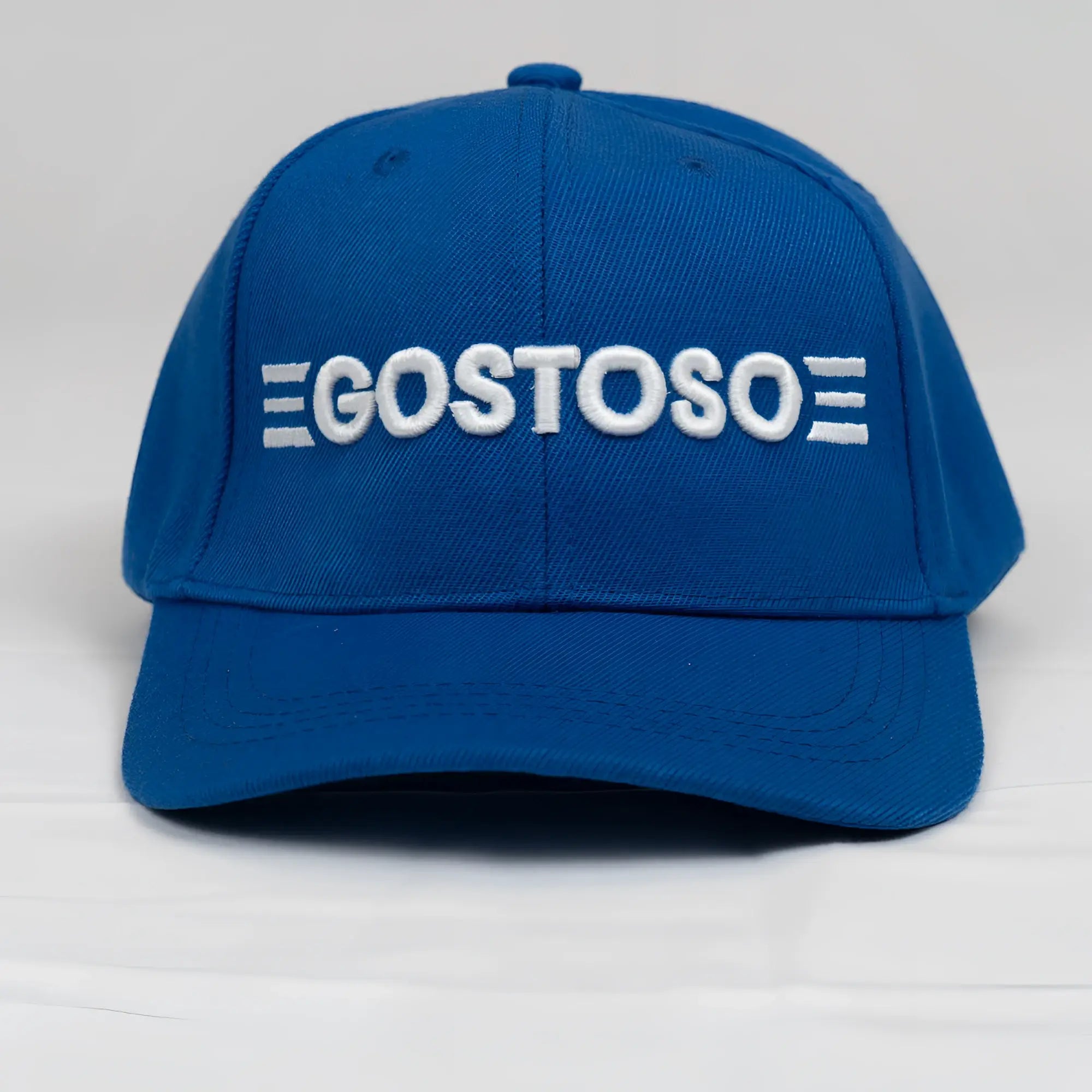 A vibrant royal blue baseball hat with bold white 3D puff gostoso stripes logo embroidered on the front