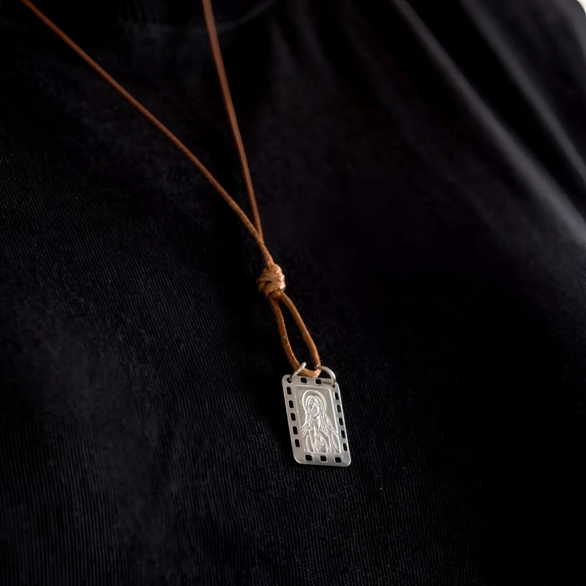 Silver rectangular Nossa Senhora do Carmo scapular pendant with engraved figure and perforated edges on brown leather cord