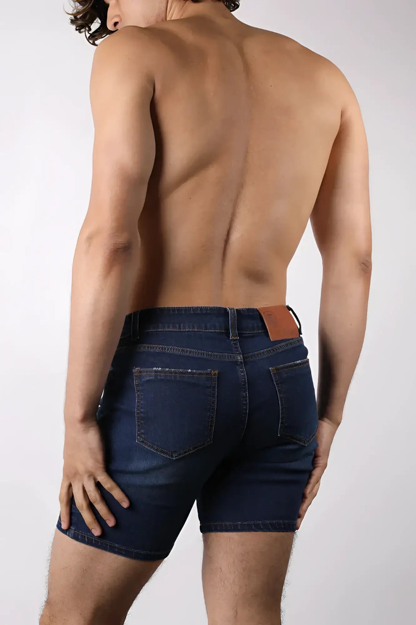 Back side of oceanside denim short showing dark blue denim with a brown leather back pocket tab