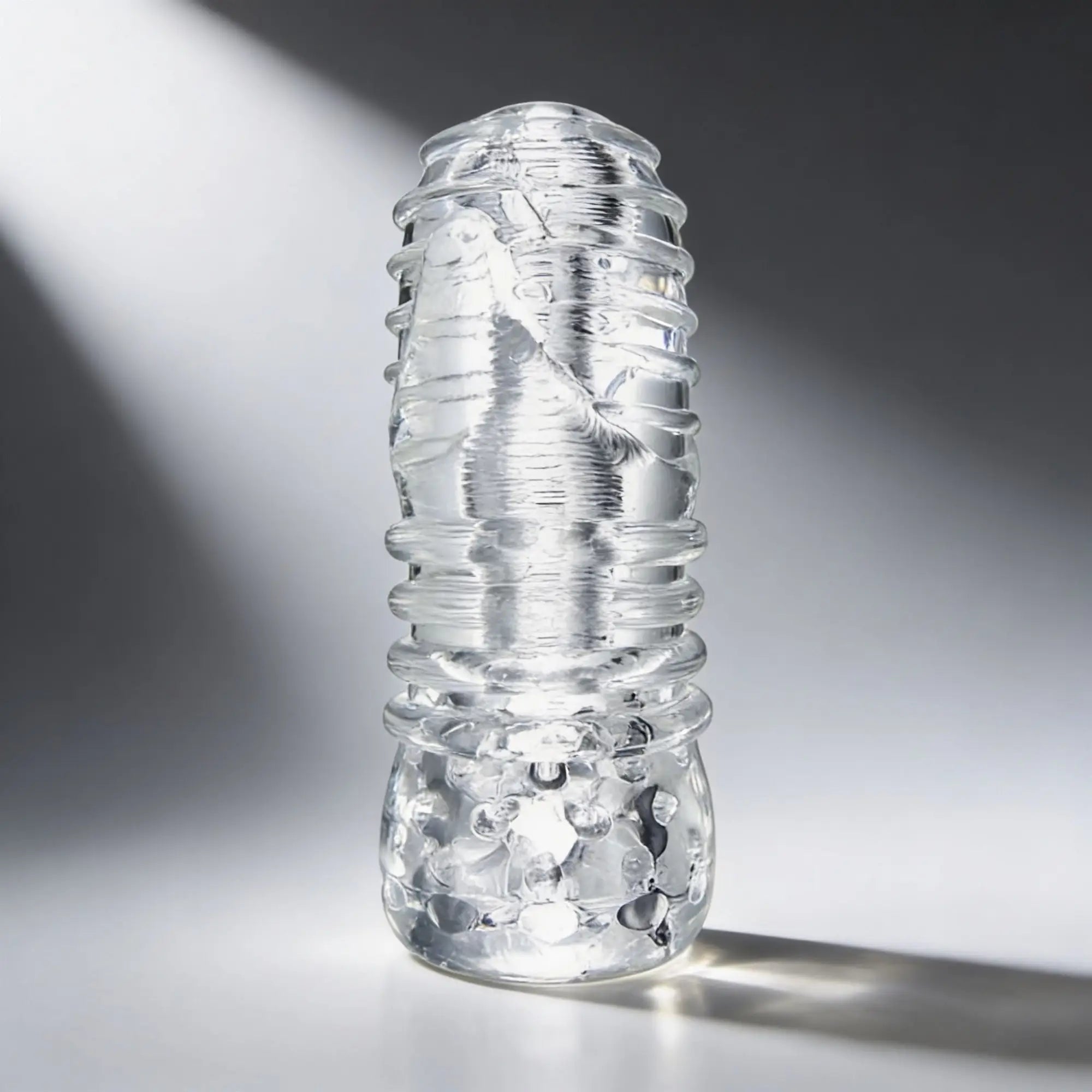 Palm-Tec LX20 Intense Stroker: A clear, ridged cylindrical sleeve with internal textured patterns, set on a white base.