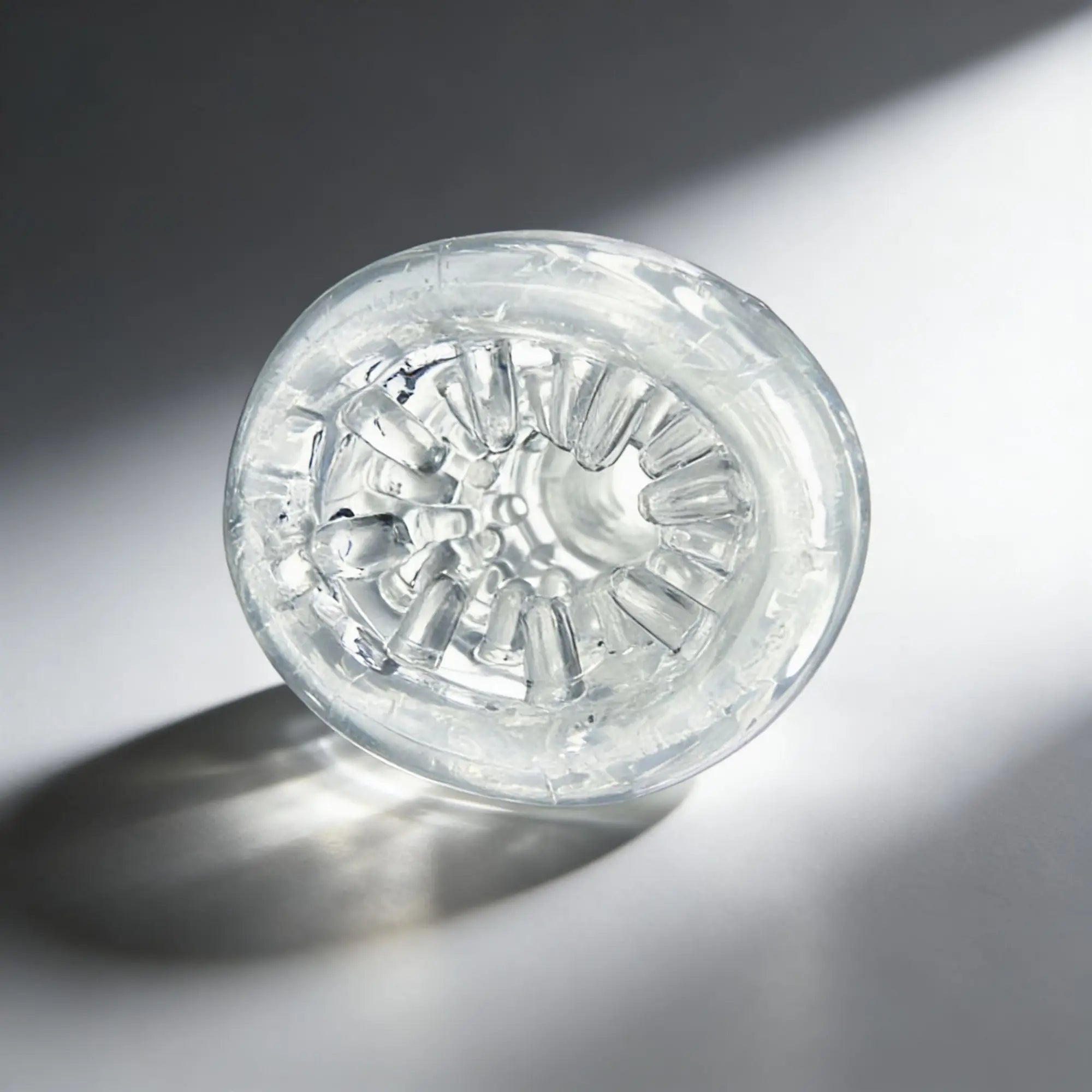 Palm-Tec LX20 Intense Stroker: A clear, textured silicone sleeve with internal ridges, shown top-down on a gray surface.