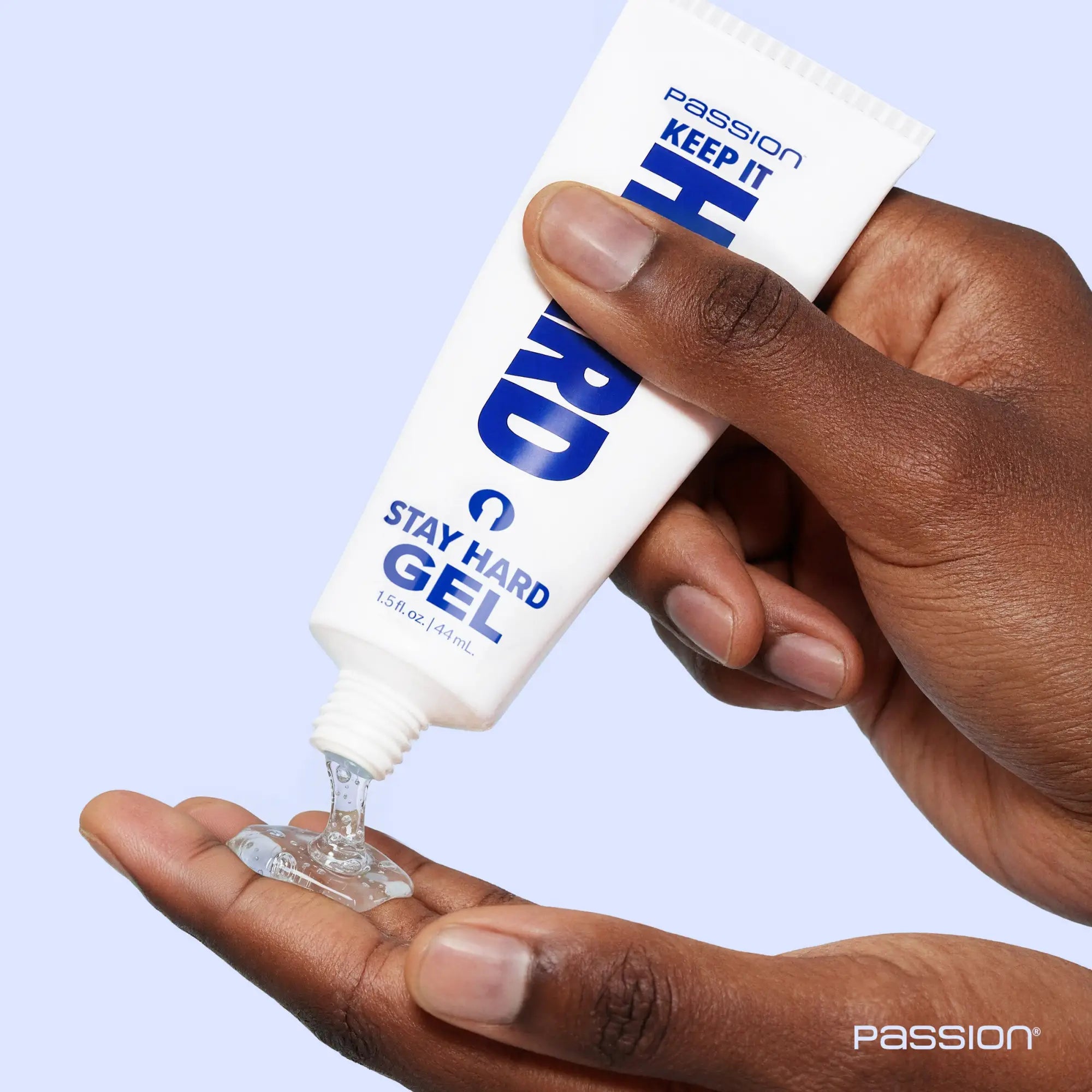 A hand squeezes clear gel from a white and blue Passion Keep It Hard Stay Hard Gel tube onto a palm.