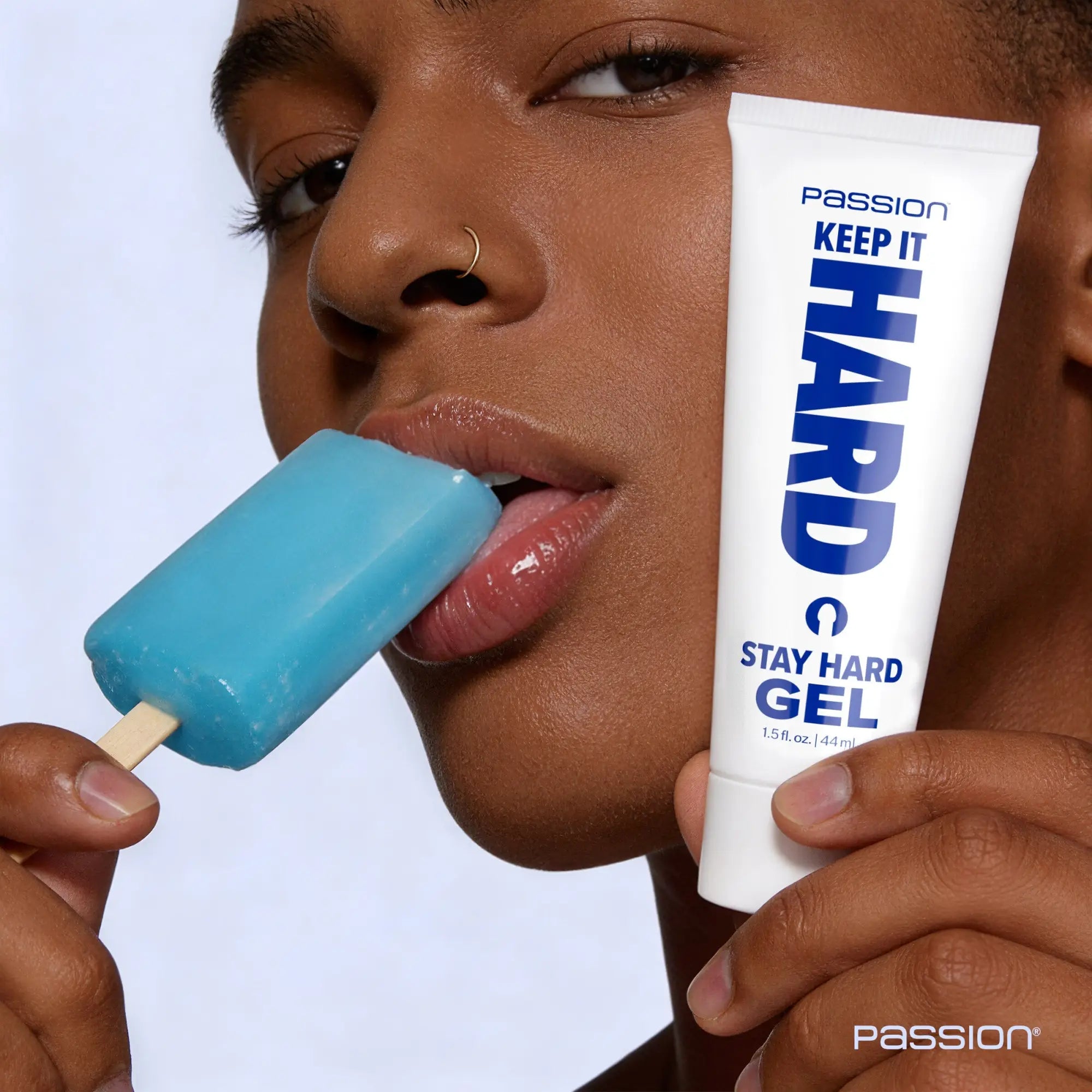 A person holds a white tube of Passion Keep It Hard Stay Hard Gel next to a blue popsicle they are eating.