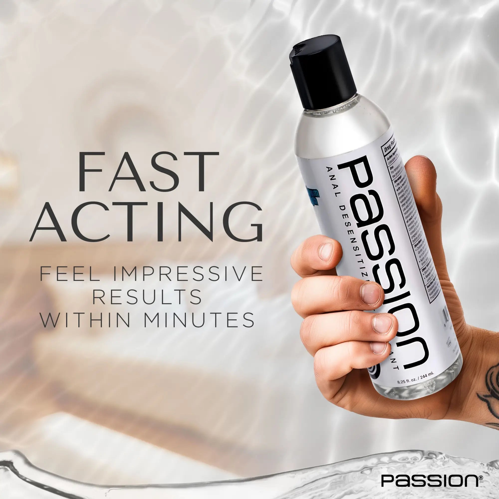 Hand holding a clear bottle of Passion Maximum Strength Anal Desensitizing Lube with a black cap against a water background.
