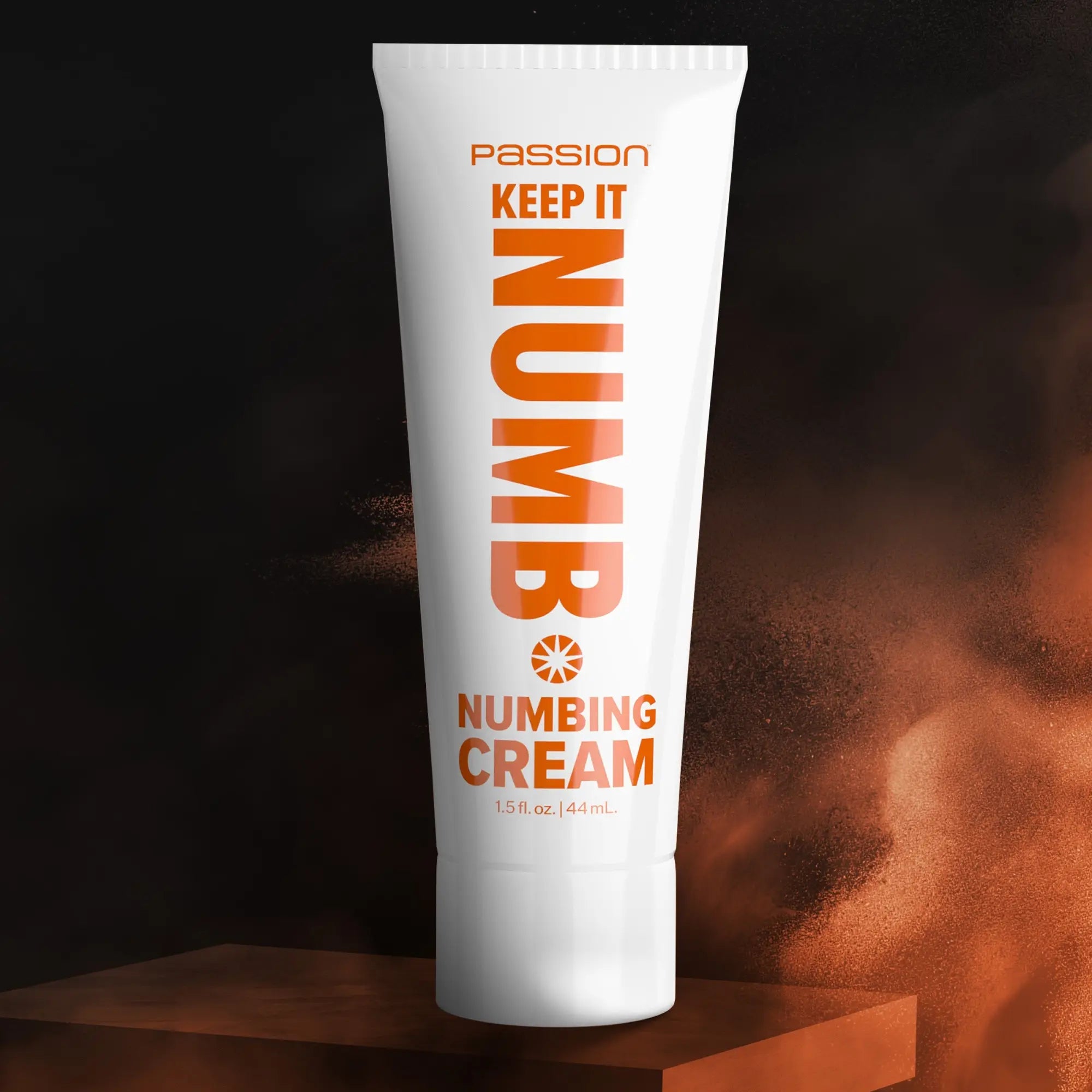White squeeze tube of Passion Keep It Numb Numbing Cream with orange text on a dark, smoky background.