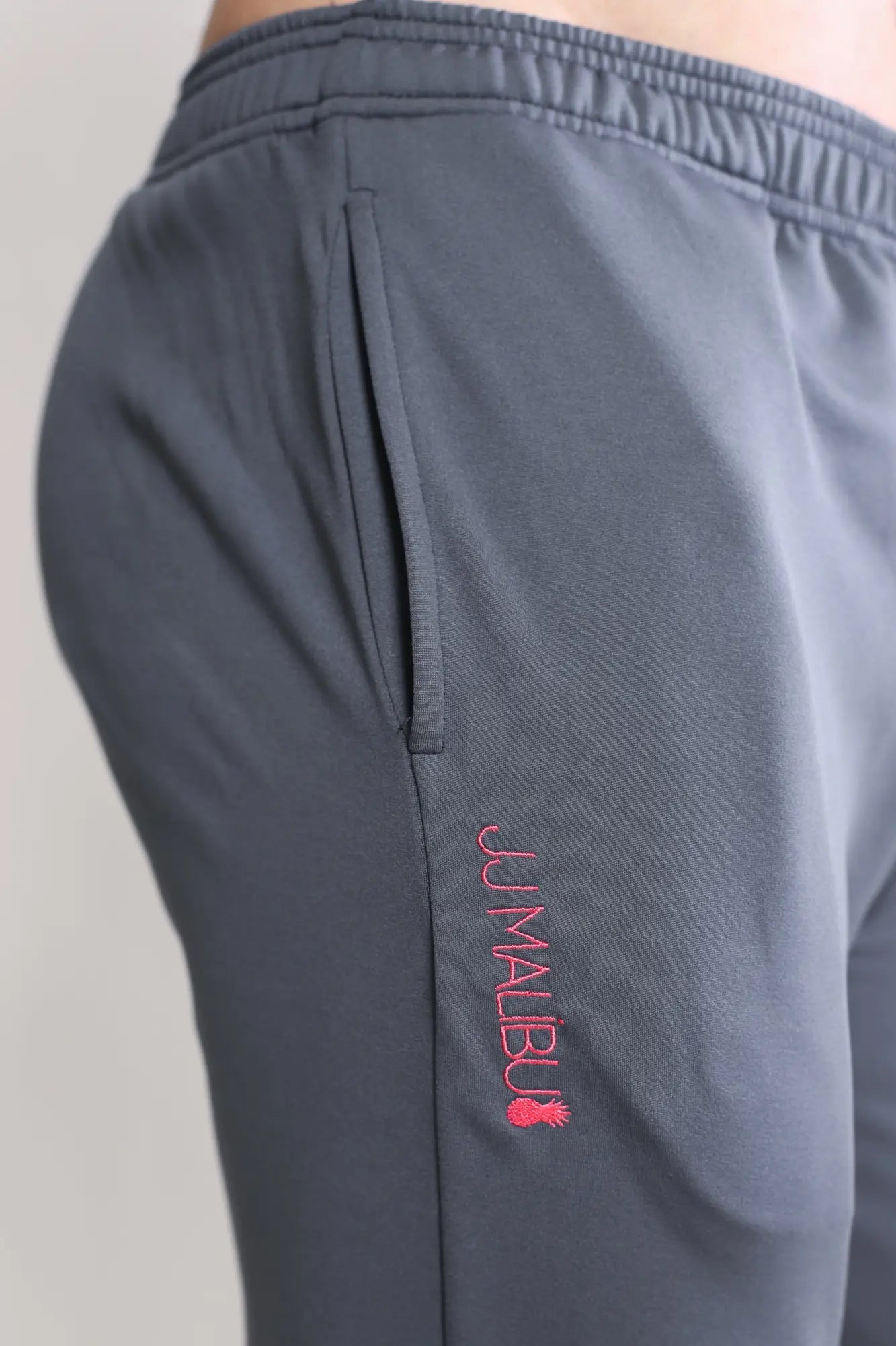 Dark grey peek-a-boo joggers with gray athletic fabric and pink jumalbu logo embroidered on the side seam