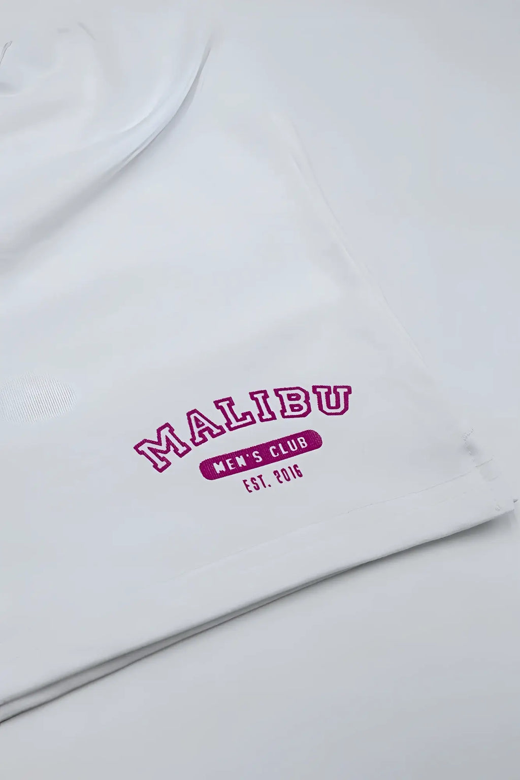 White cotton t-shirt with bold pink embroidered malibu men’s club est logo paired with peek-a-boo varsity marshmallow shorts