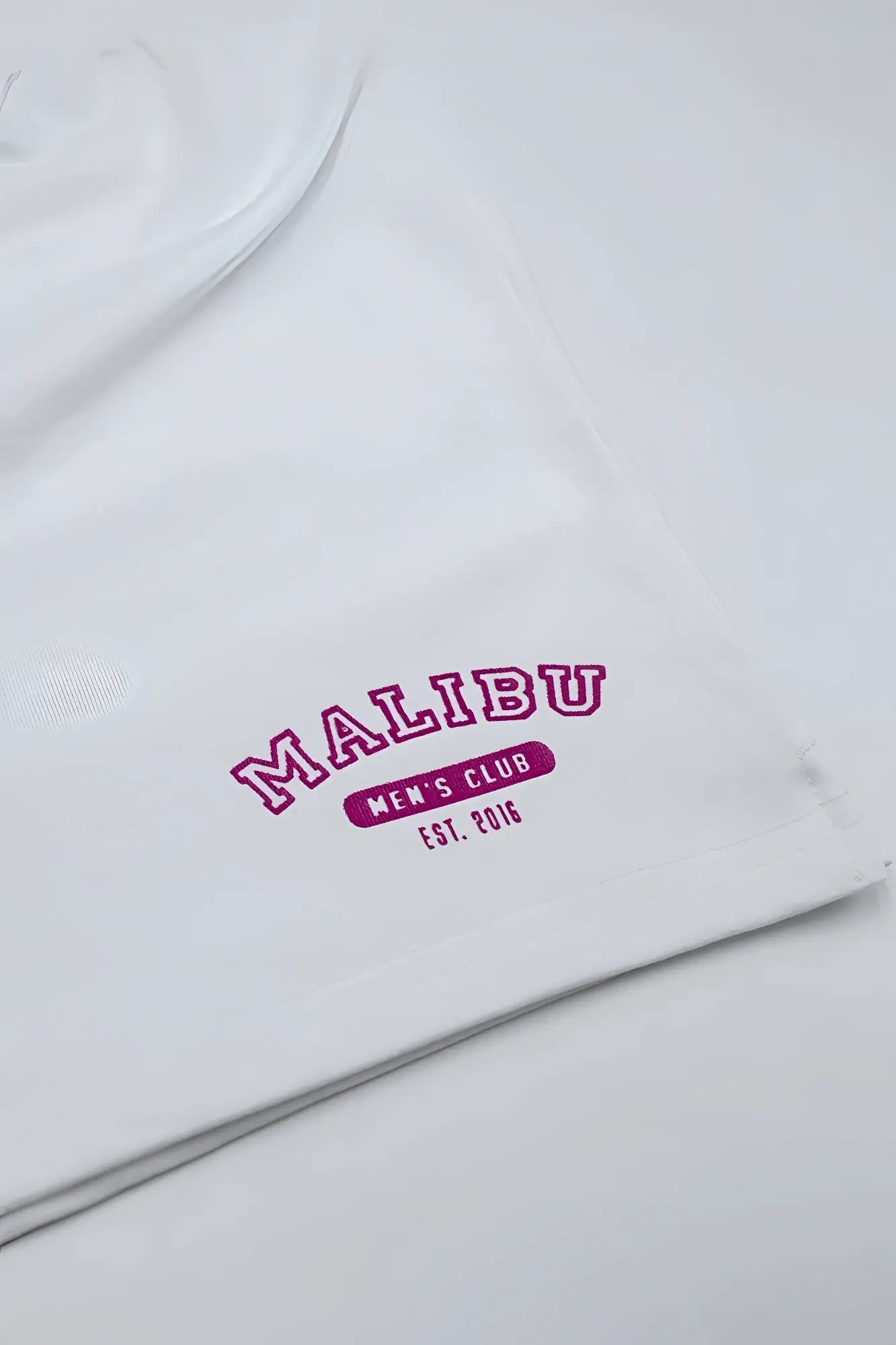 White cotton t-shirt with bold pink embroidered malibu men’s club est logo paired with peek-a-boo varsity marshmallow shorts