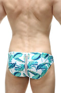 White swim trunks with vibrant teal and green tropical leaf pattern and central gray zipper petitq swim bikini tarcu macouba