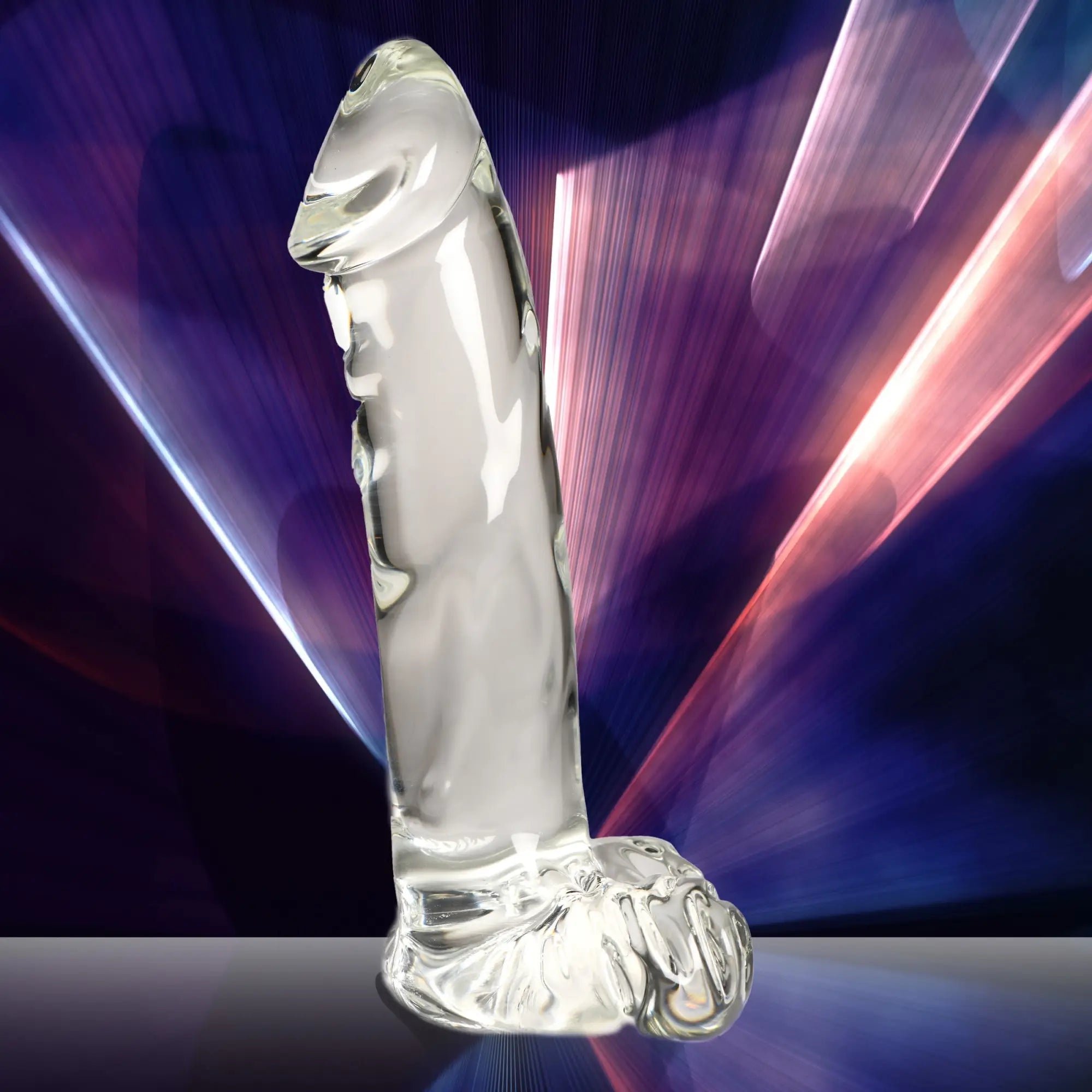 Pleasure Crystals clear glass dildo with integrated balls, set against a dark purple and pink light-streaked background.