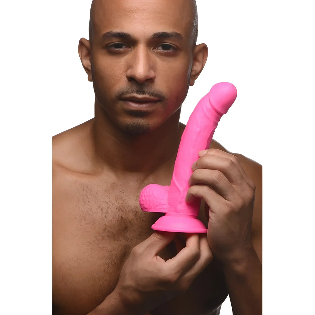 A man holds a bright pink, 7.5-inch curved Pop Peckers dildo with realistic balls and a suction-cup base.
