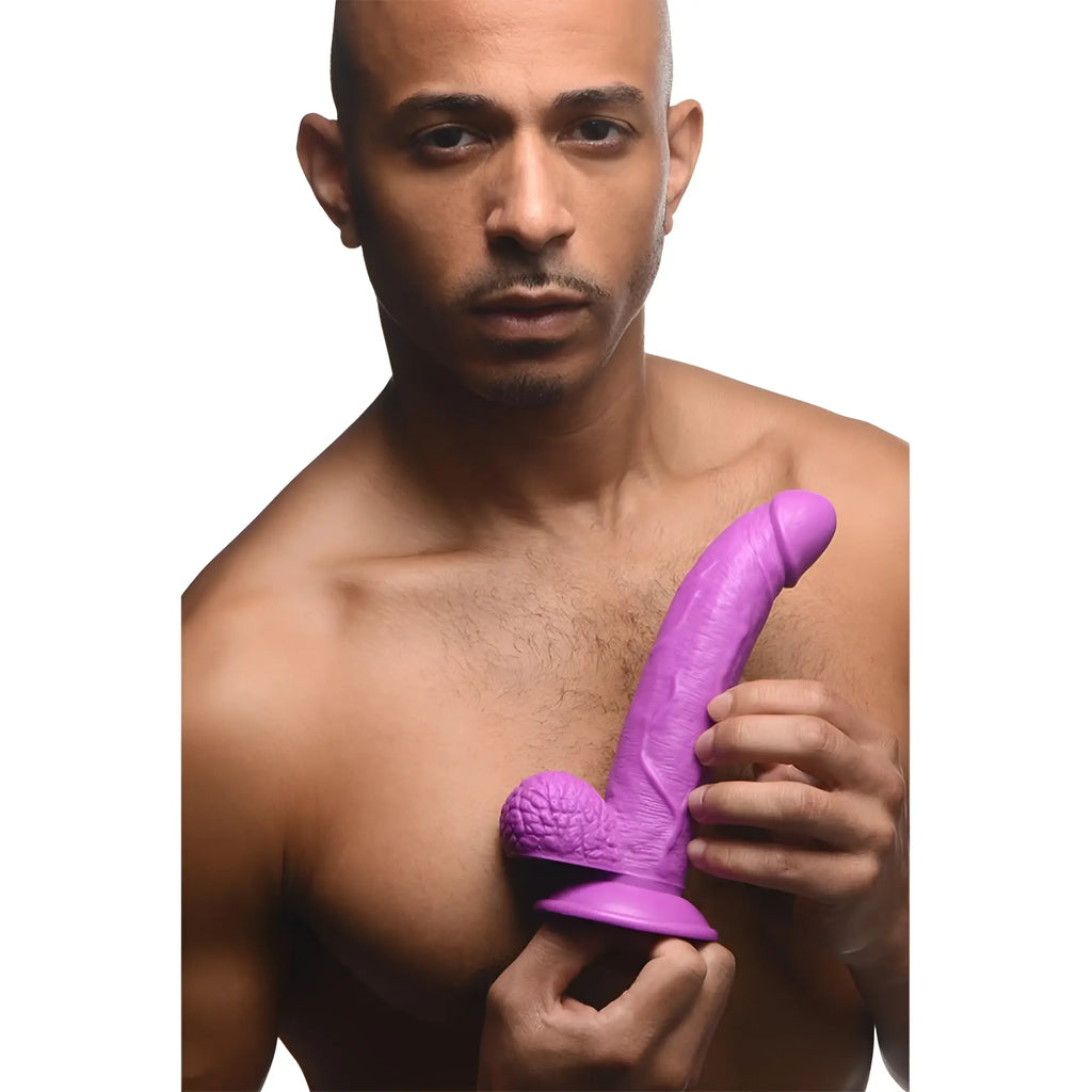Man holding a 7.5-inch purple Pop Peckers curved dildo featuring realistic texture and balls.