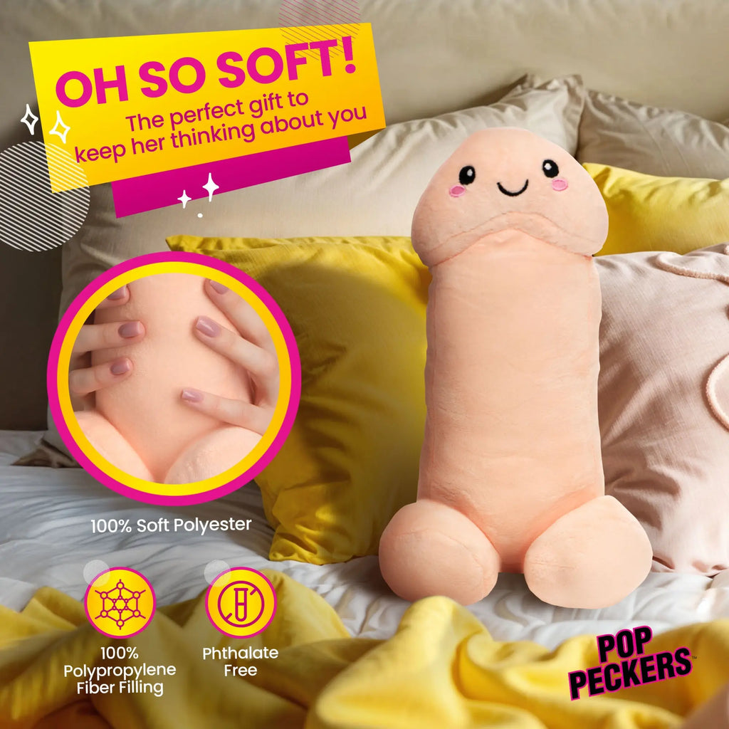 Pop Peckers Happy Peckers penis-shaped plush pillow in soft beige with a cute smiling face on a bed with yellow pillows.