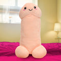 Pop Peckers Happy Peckers penis-shaped plush pillow in light peach with a cute, smiling face on a pink bedspread.