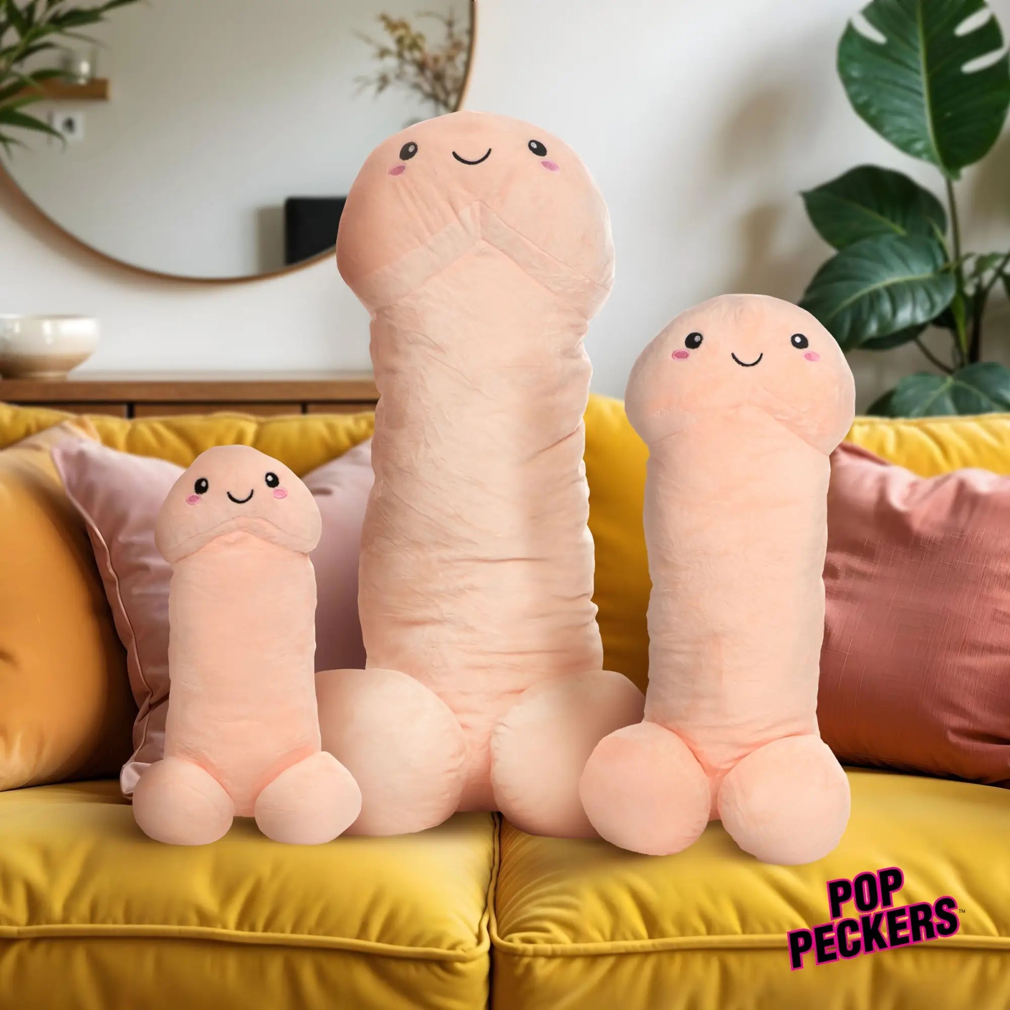 Three light pink, plush Happy Peckers pillows with embroidered smiley faces, sitting on a yellow sofa.