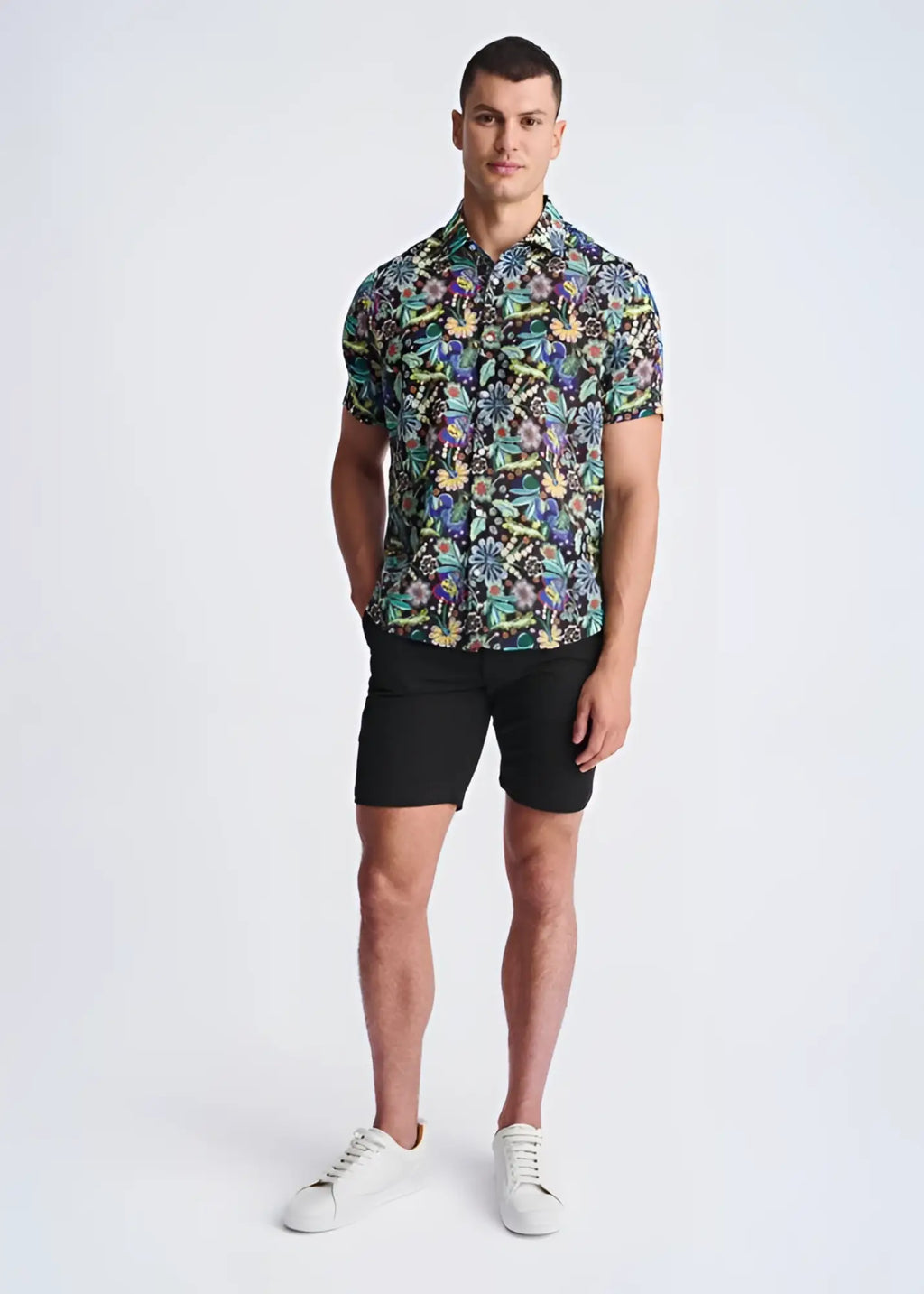 A man wearing a floral lightweight linen tencel short-sleeved shirt with a multicolored pattern on a dark background