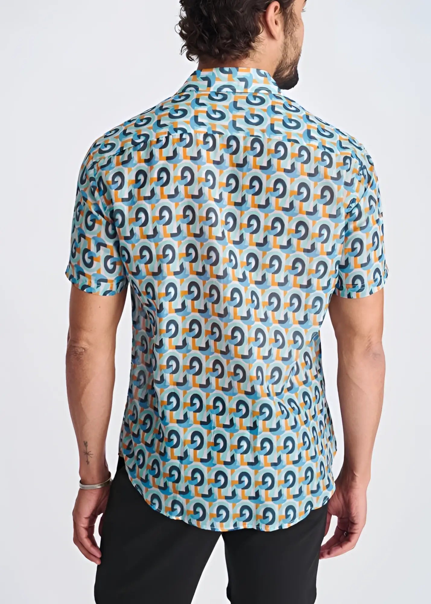 A man wearing a swirls lightweight cotton silk short-sleeved shirt with blue and orange geometric pattern on turquoise