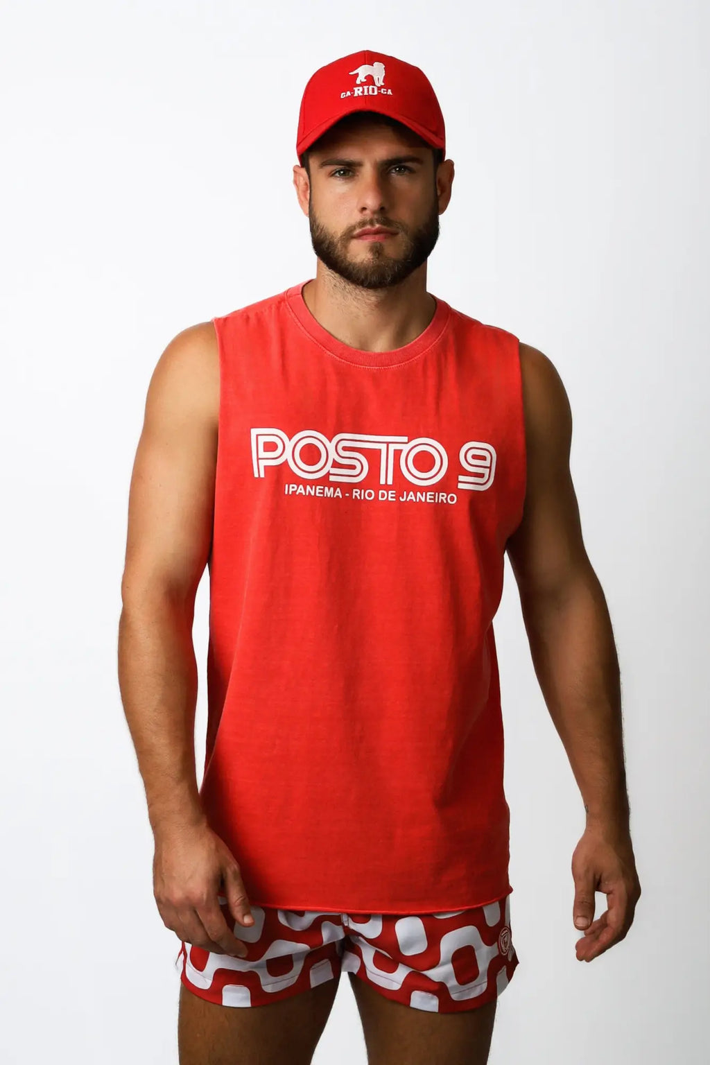 Man wearing a red sleeveless tank top with white posto 9 lettering and smaller text below in a posto 9 ipanema tee