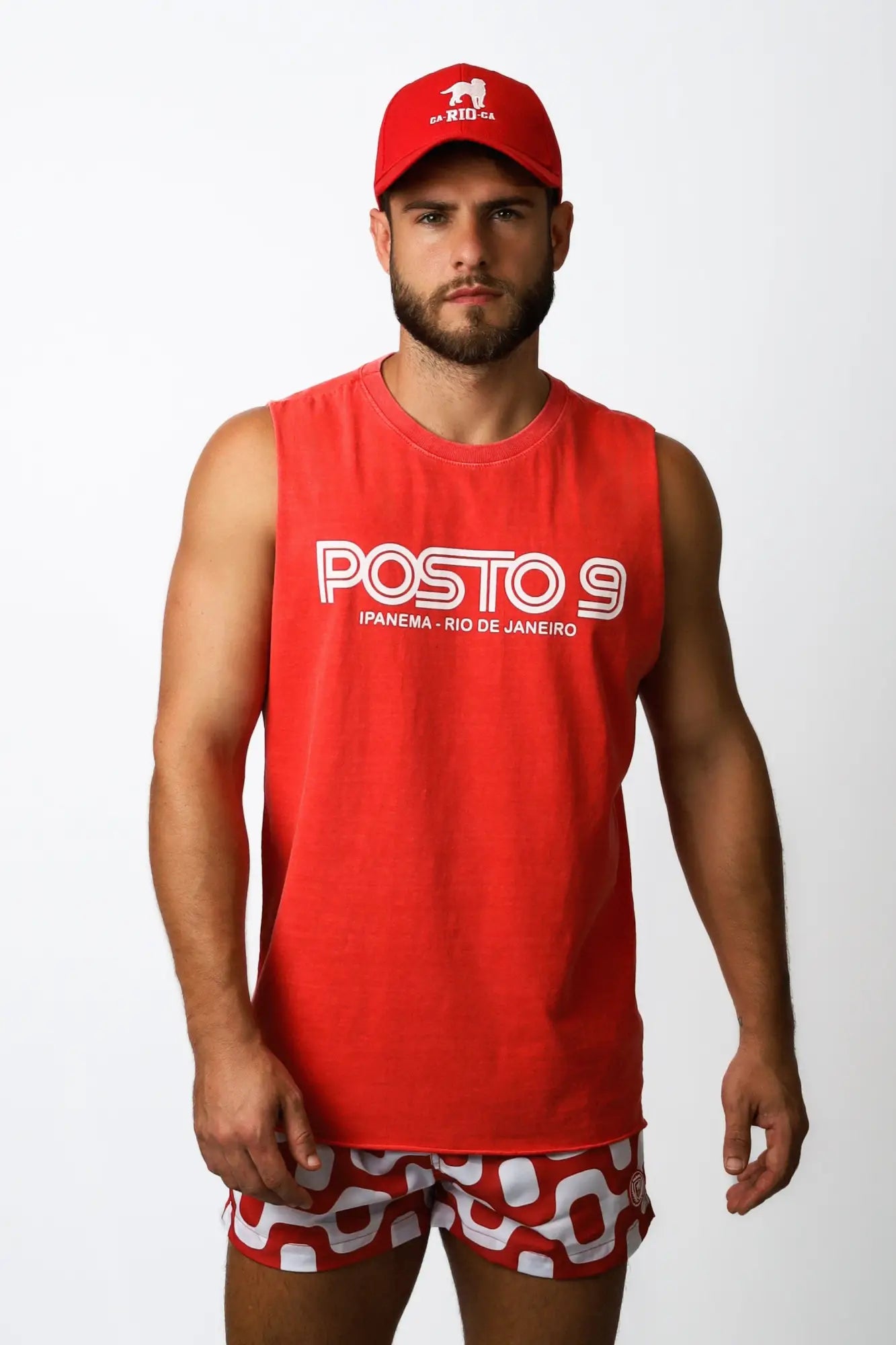 Man wearing a red sleeveless tank top with white posto 9 lettering and smaller text below in a posto 9 ipanema tee