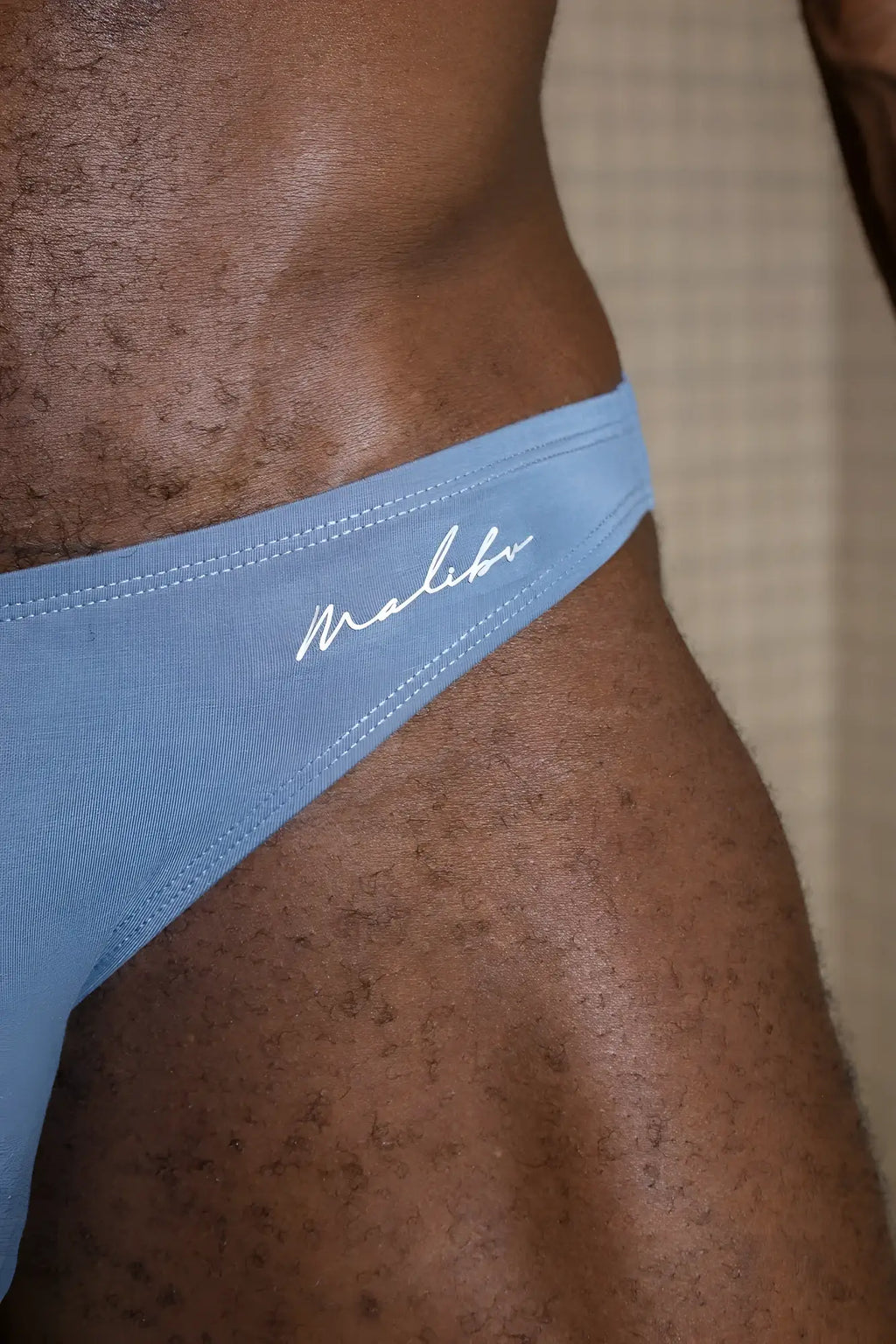 Premium modal scrunch-back cheeky brief in dusty blue with light blue Malibu thong and white cursive logo stitching visible